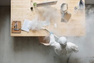 Osoba w kombinezonie ochronnym odkażająca stół
