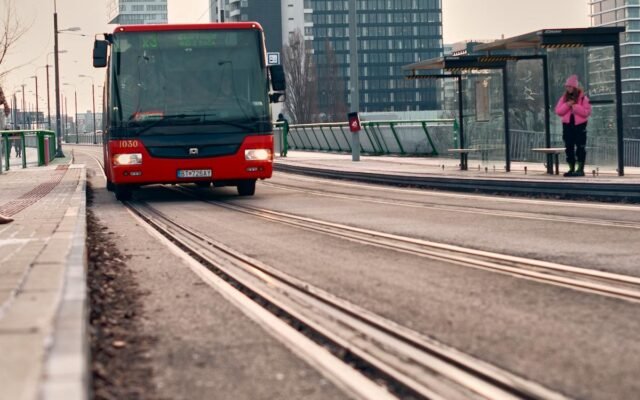 Miejski przystanek tramwajowy z czerwonym autobusem i widokiem na miasto